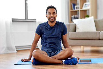 Image showing smiling indian man sitting on exercise mat at home