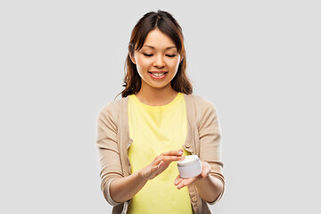 Image showing happy young asian woman holding jar of moisturizer