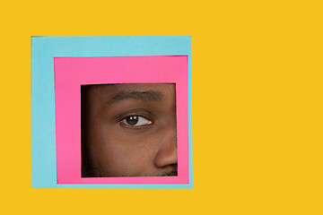 Image showing Eye of african-american man peeking throught square in yellow background