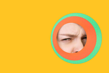 Image showing Female eye peeking throught circle in yellow background