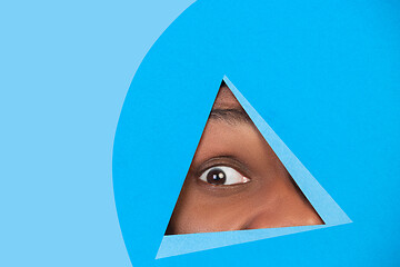 Image showing Eye of african-american man peeking throught triangle in blue background