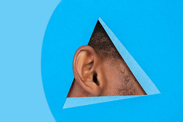 Image showing Ear of african-american man peeking throught triangle in blue background