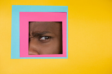 Image showing Eye of african-american man peeking throught square in yellow background