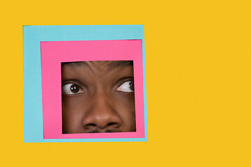 Image showing Face of african-american man peeking throught square in yellow background