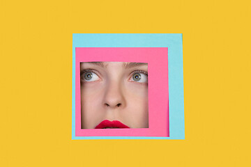 Image showing Face of caucasian woman peeking throught square in yellow background