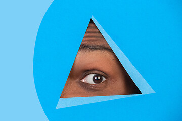 Image showing Eye of african-american man peeking throught triangle in blue background