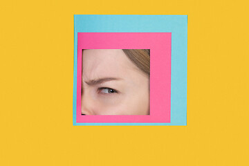 Image showing Face of caucasian woman peeking throught square in yellow background