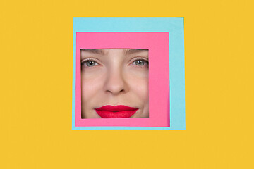 Image showing Face of caucasian woman peeking throught square in yellow background