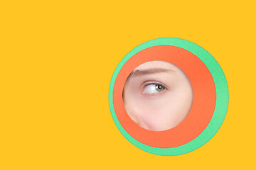 Image showing Female eye peeking throught circle in yellow background