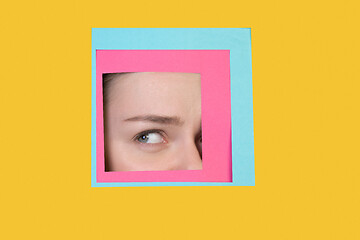 Image showing Face of caucasian woman peeking throught square in yellow background