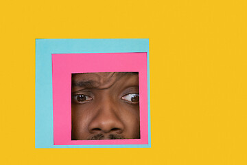 Image showing Face of african-american man peeking throught square in yellow background