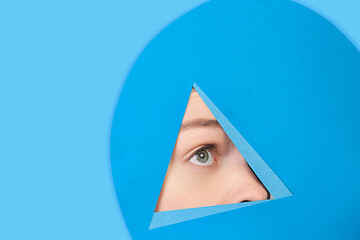 Image showing Face of caucasian woman peeking throught triangle in blue background