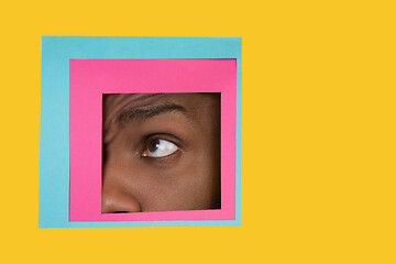 Image showing Eye of african-american man peeking throught square in yellow background