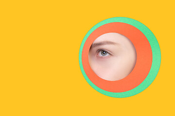 Image showing Female eye peeking throught circle in yellow background