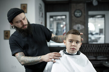 Image showing Children hairdresser cutting little boy against a dark background.