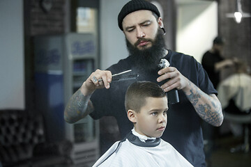 Image showing Children hairdresser cutting little boy against a dark background.