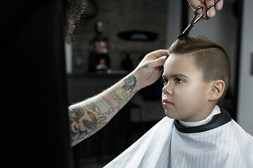 Image showing Children hairdresser cutting little boy against a dark background.