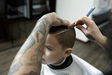 Image showing Children hairdresser cutting little boy against a dark background.