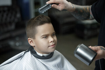 Image showing Children hairdresser cutting little boy against a dark background.