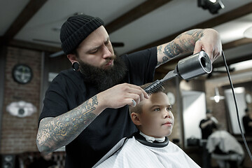 Image showing Children hairdresser cutting little boy against a dark background.