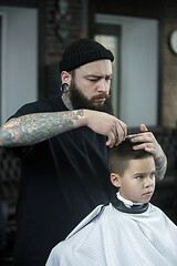 Image showing Children hairdresser cutting little boy against a dark background.