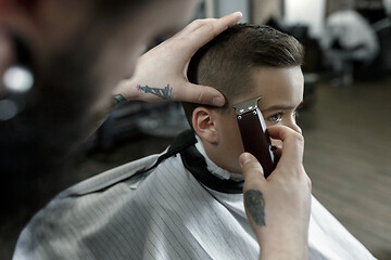 Image showing Children hairdresser cutting little boy against a dark background.