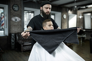 Image showing Children hairdresser cutting little boy against a dark background.