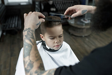 Image showing Children hairdresser cutting little boy against a dark background.