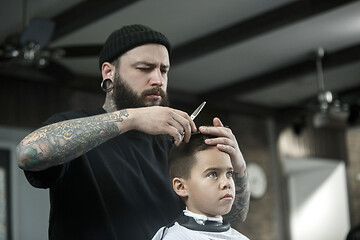 Image showing Children hairdresser cutting little boy against a dark background.