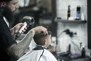 Image showing Children hairdresser cutting little boy against a dark background.