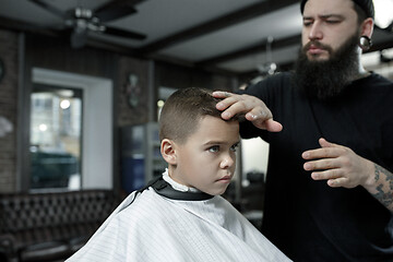 Image showing Children hairdresser cutting little boy against a dark background.