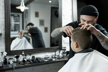 Image showing Children hairdresser cutting little boy against a dark background.