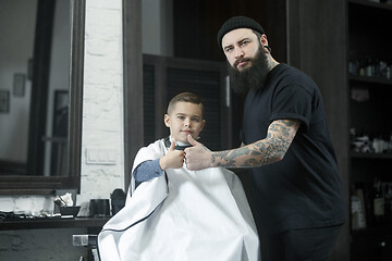 Image showing Children hairdresser cutting little boy against a dark background.