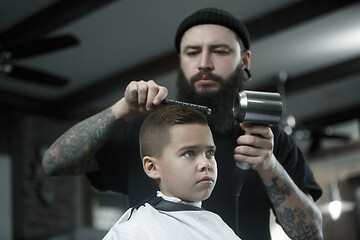 Image showing Children hairdresser cutting little boy against a dark background.