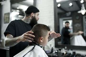 Image showing Children hairdresser cutting little boy against a dark background.