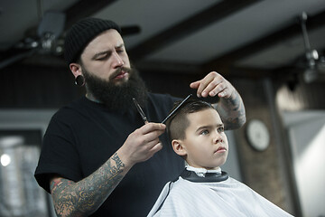 Image showing Children hairdresser cutting little boy against a dark background.