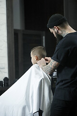 Image showing Children hairdresser cutting little boy against a dark background.