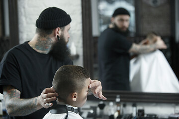 Image showing Children hairdresser cutting little boy against a dark background.