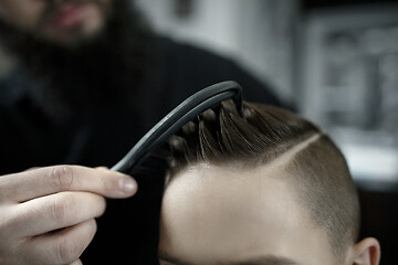 Image showing Children hairdresser cutting little boy against a dark background.