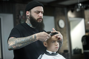 Image showing Children hairdresser cutting little boy against a dark background.