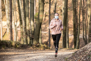 Image showing Corona virus, or Covid-19, is spreading all over the world. Portrait of caucasian sporty woman wearing a medical protection face mask while running in nature.