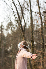 Image showing Portrait of caucasian sporty woman wearing medical protection face mask while relaxing by taking a deep breath in forest. Corona virus, or Covid-19, is spreading all over the world