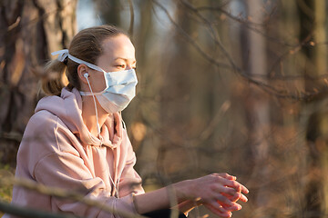 Image showing Portrait of caucasian sporty woman wearing medical protection face mask while relaxing in nature and listening to music. Corona virus, or Covid-19, is spreading all over the world