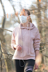 Image showing Portrait of caucasian sporty woman wearing medical protection face mask while walking in park, relaxing and listening to music. Corona virus, or Covid-19, is spreading all over the world