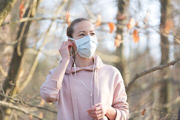 Image showing Portrait of caucasian sporty woman wearing medical protection face mask while walking in park, relaxing and listening to music. Corona virus, or Covid-19, is spreading all over the world