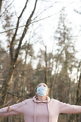 Image showing Portrait of caucasian sporty woman wearing medical protection face mask while relaxing by taking a deep breath in forest. Corona virus, or Covid-19, is spreading all over the world