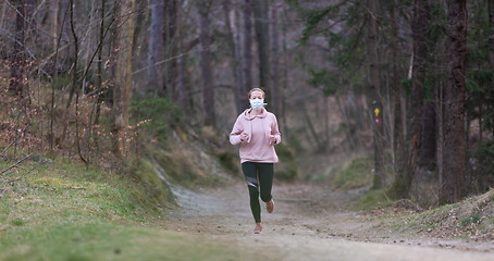 Image showing Corona virus, or Covid-19, is spreading all over the world. Portrait of caucasian sporty woman wearing a medical protection face mask while running in nature.