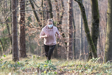 Image showing Corona virus, or Covid-19, is spreading all over the world. Portrait of caucasian sporty woman wearing a medical protection face mask while running in nature.