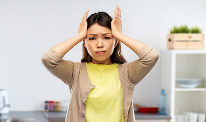 Image showing stressed asian woman holding to head at kitchen