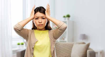 Image showing stressed asian woman holding to her head at home